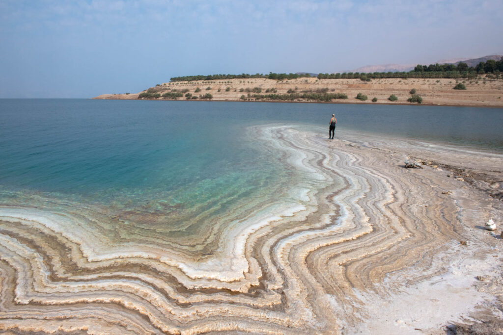 Vrouw kijkt vanaf zoutafzettingen uit over de Dode Zee